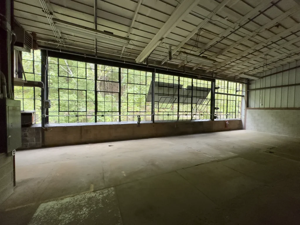 Large, unfinished industrial space with windows opening to a natural spring feed river