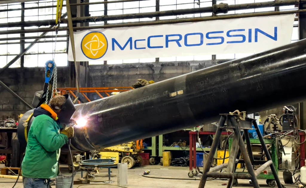 welding a large steel pipe in front of a McCrossin banner